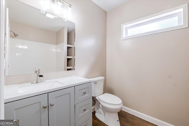 bathroom featuring toilet, wood finished floors, vanity, baseboards, and walk in shower