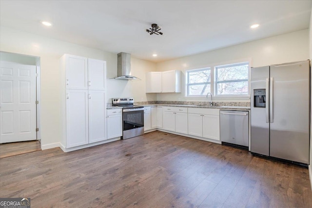 kitchen with wood finished floors, stainless steel appliances, wall chimney range hood, white cabinetry, and a sink