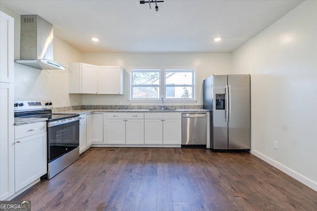 kitchen featuring wall chimney range hood, a sink, appliances with stainless steel finishes, and white cabinetry