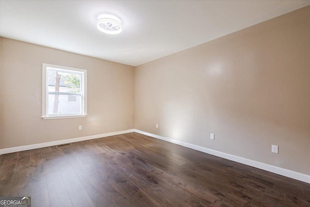 empty room with visible vents, dark wood finished floors, and baseboards