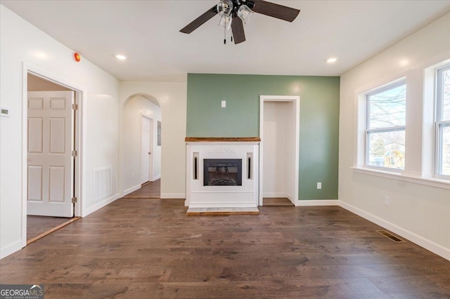 unfurnished living room with baseboards, visible vents, arched walkways, and wood finished floors