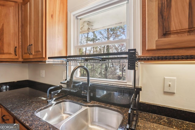 kitchen featuring dark stone counters, brown cabinets, and a sink