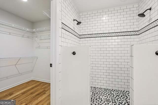 bathroom with a spacious closet, baseboards, a walk in shower, and wood finished floors