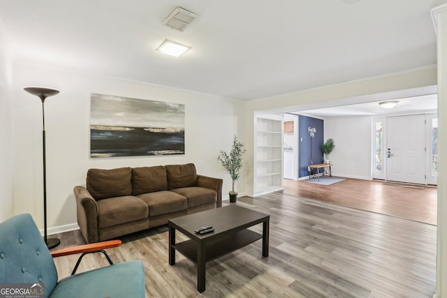 living area with baseboards, wood finished floors, visible vents, and crown molding