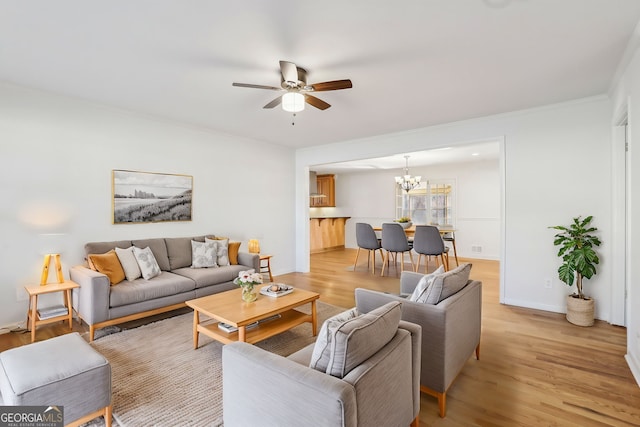 living room with light wood-type flooring, baseboards, ornamental molding, and ceiling fan with notable chandelier