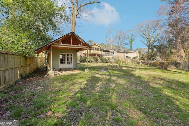 rear view of house with a fenced backyard, stairway, an outbuilding, a yard, and french doors