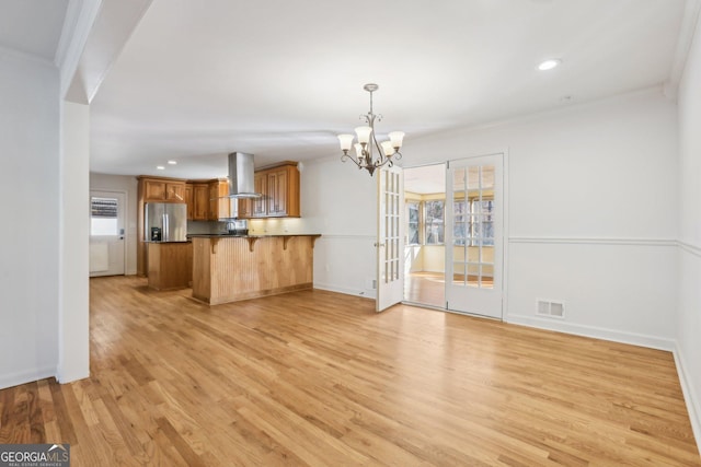 kitchen featuring brown cabinets, stainless steel refrigerator with ice dispenser, a peninsula, a kitchen bar, and exhaust hood