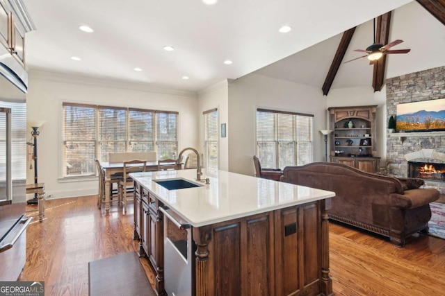 kitchen featuring a fireplace, light countertops, lofted ceiling with beams, a sink, and light wood-type flooring