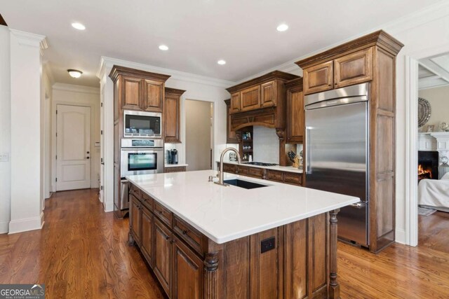 kitchen featuring dark wood-style flooring, a sink, a lit fireplace, and built in appliances