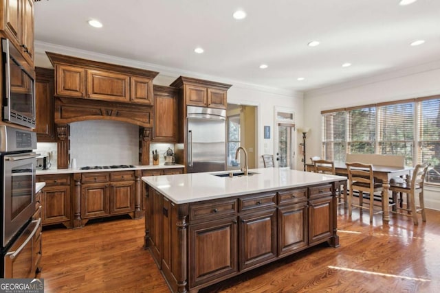 kitchen featuring wood finished floors, light countertops, a sink, and built in appliances