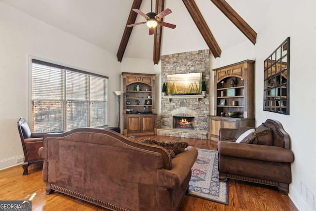 living room featuring a stone fireplace, wood finished floors, visible vents, and baseboards