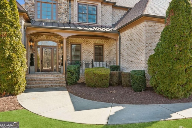 property entrance featuring a shingled roof, metal roof, a standing seam roof, a porch, and brick siding