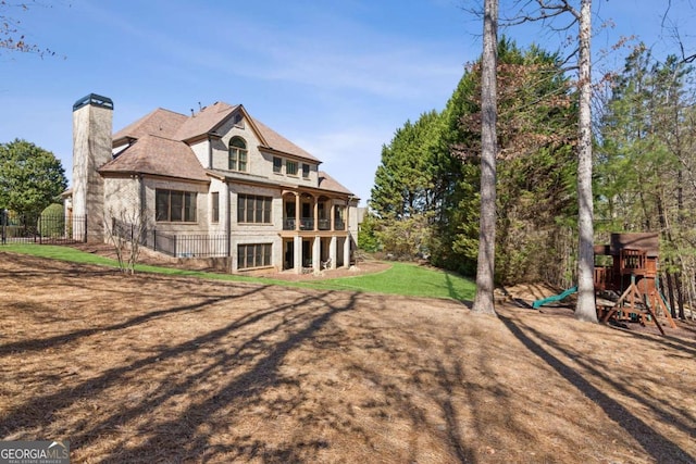 rear view of property with a chimney, a playground, fence, and a lawn