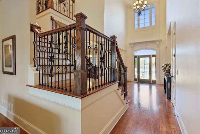 foyer entrance with baseboards, visible vents, wood finished floors, a high ceiling, and a notable chandelier