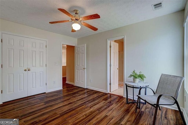 living area with visible vents, a textured ceiling, baseboards, and wood finished floors