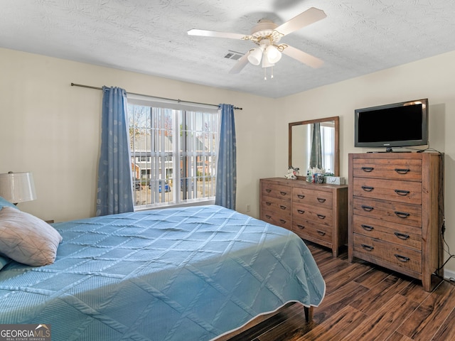 bedroom with dark wood-style flooring, visible vents, ceiling fan, and a textured ceiling