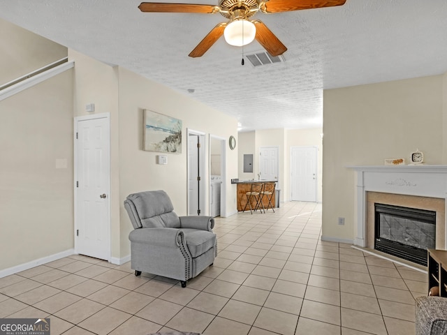 sitting room featuring visible vents, a glass covered fireplace, a textured ceiling, and light tile patterned flooring