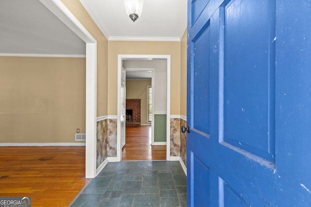 entrance foyer with a wainscoted wall, a fireplace, crown molding, visible vents, and wood finished floors