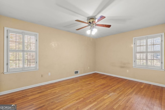 spare room with baseboards, light wood-style floors, visible vents, and a healthy amount of sunlight