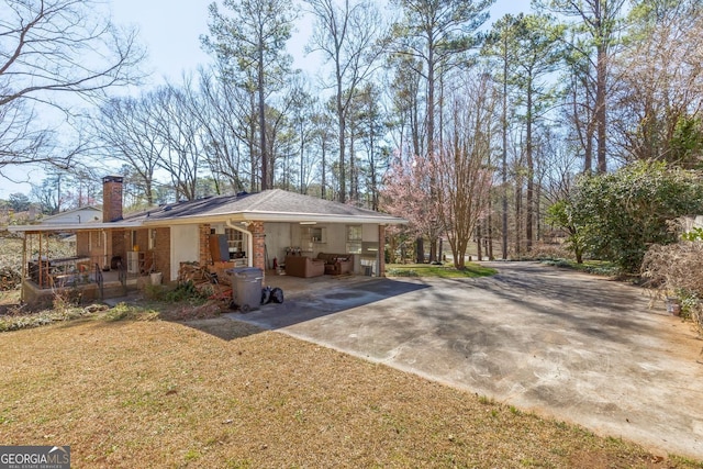 view of front of home featuring concrete driveway, a chimney, covered porch, a front yard, and brick siding