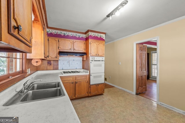 kitchen with crown molding, light countertops, a sink, under cabinet range hood, and baseboards