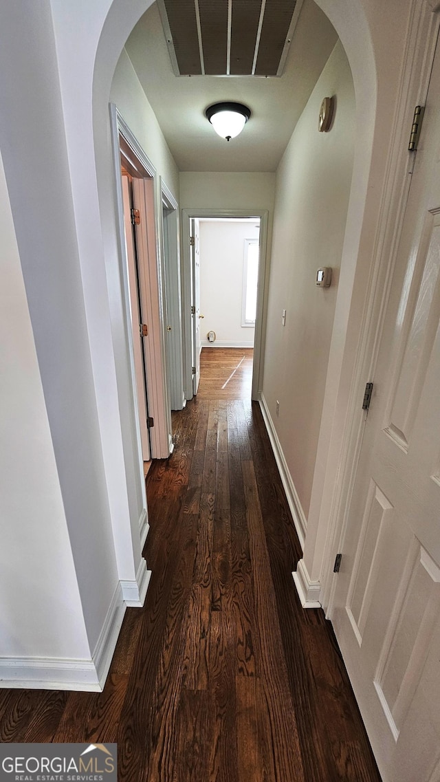 hallway with baseboards, arched walkways, and dark wood-type flooring