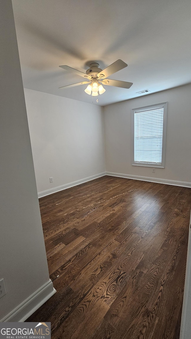 spare room with dark wood-style floors, baseboards, visible vents, and a ceiling fan