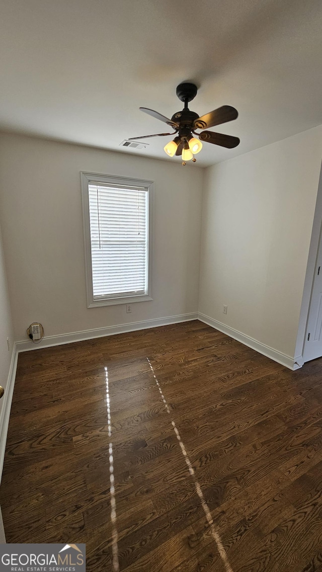 unfurnished room with dark wood-style flooring, visible vents, and baseboards