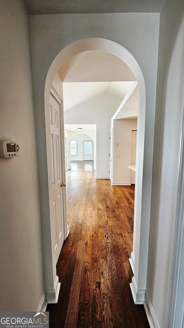 hall featuring lofted ceiling, arched walkways, baseboards, and wood finished floors