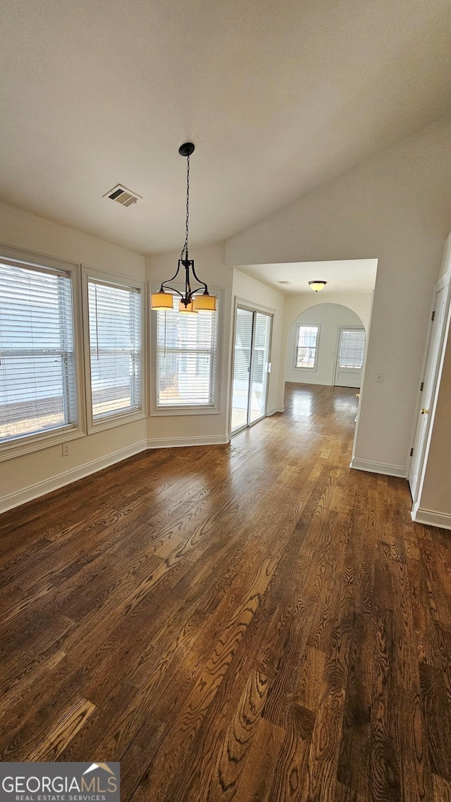 unfurnished dining area featuring dark wood-style floors, arched walkways, lofted ceiling, visible vents, and baseboards