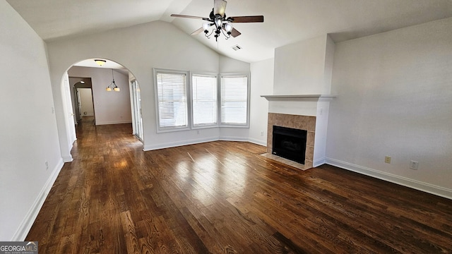 unfurnished living room featuring arched walkways, a ceiling fan, a tile fireplace, dark wood-style flooring, and vaulted ceiling