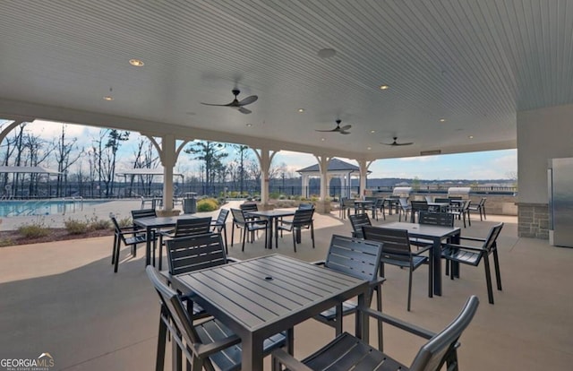 view of patio featuring outdoor dining area, fence, a ceiling fan, and a community pool