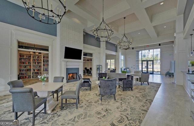 dining room with a warm lit fireplace, coffered ceiling, beamed ceiling, a high ceiling, and a chandelier