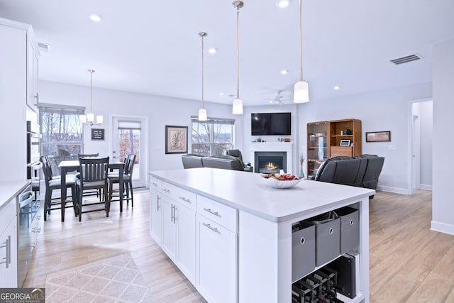 kitchen with light wood finished floors, visible vents, a kitchen island, a lit fireplace, and light countertops