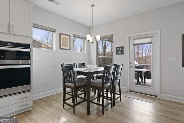 dining space featuring light wood-type flooring, visible vents, a notable chandelier, and baseboards