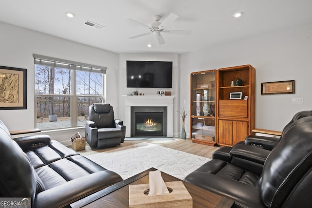 living area with recessed lighting, visible vents, a ceiling fan, a glass covered fireplace, and wood finished floors