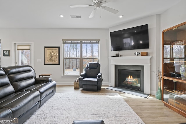 living area with a healthy amount of sunlight, visible vents, wood finished floors, and a glass covered fireplace