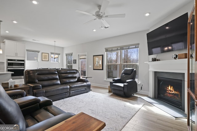 living room with recessed lighting, a warm lit fireplace, and light wood-style flooring