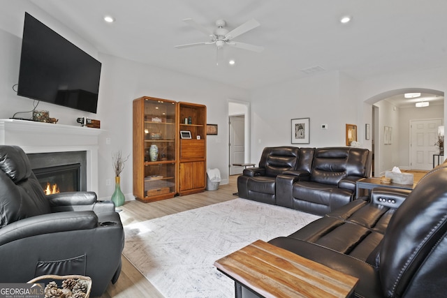 living room featuring arched walkways, ceiling fan, recessed lighting, light wood-style floors, and a glass covered fireplace