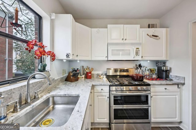 kitchen with white microwave, range with two ovens, a sink, visible vents, and white cabinets