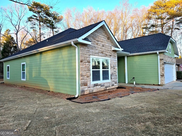 view of side of home featuring stone siding, roof with shingles, and an attached garage