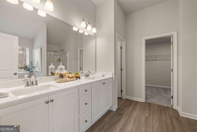 bathroom featuring double vanity, wood finished floors, a stall shower, and a sink