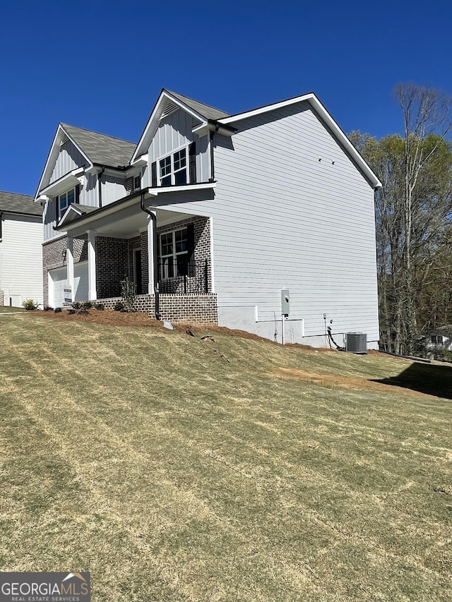 view of side of property featuring central AC unit, a lawn, board and batten siding, and brick siding