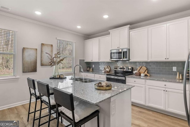 kitchen with stainless steel appliances, a sink, visible vents, light wood-style floors, and ornamental molding