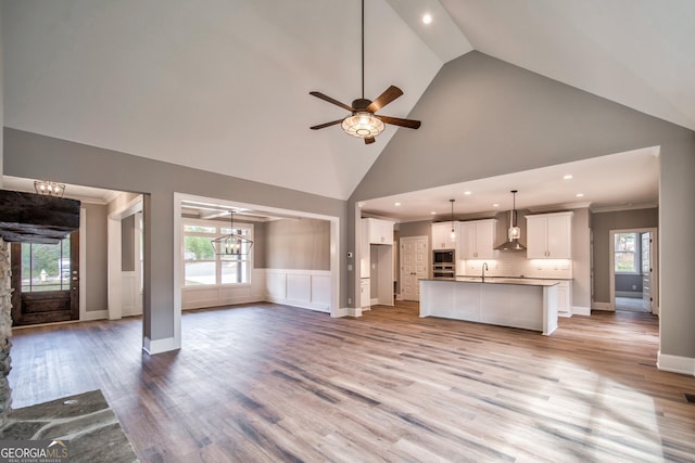 unfurnished living room featuring light wood-type flooring, ornamental molding, ceiling fan with notable chandelier, high vaulted ceiling, and a sink