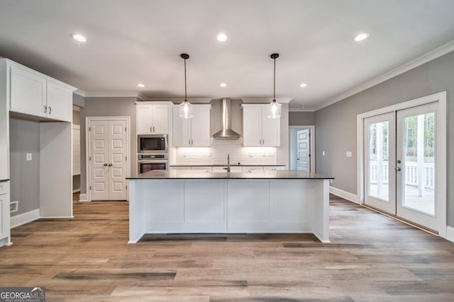 kitchen with wall chimney range hood, ornamental molding, decorative backsplash, appliances with stainless steel finishes, and white cabinetry