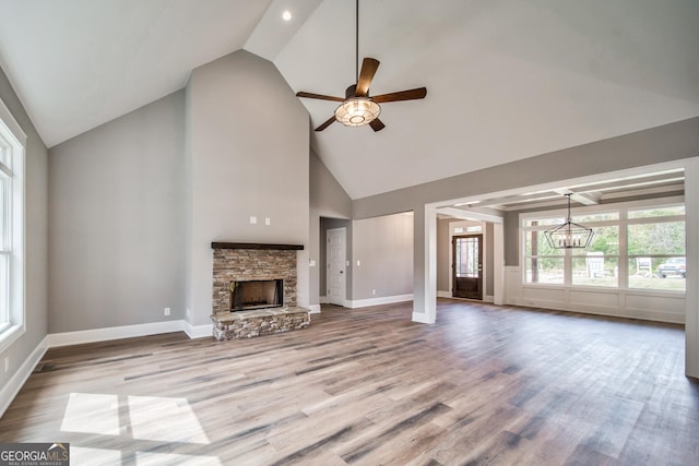 unfurnished living room featuring baseboards, a stone fireplace, wood finished floors, and ceiling fan with notable chandelier