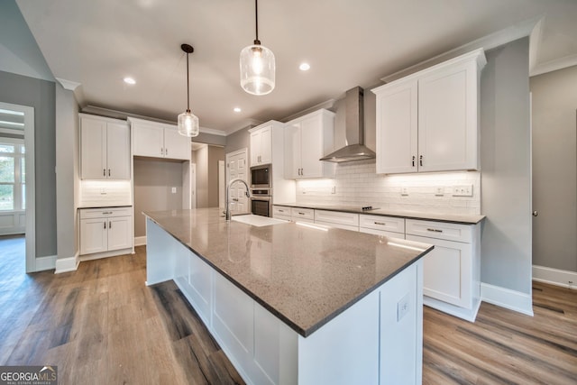 kitchen with a large island, stainless steel microwave, wall chimney exhaust hood, white cabinets, and decorative backsplash