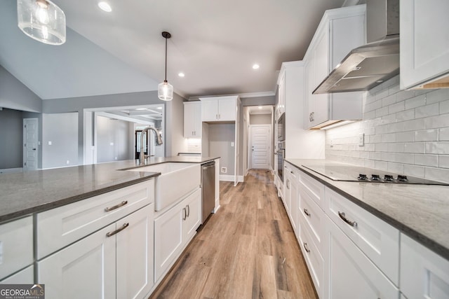 kitchen with dark stone countertops, a sink, appliances with stainless steel finishes, white cabinetry, and wall chimney range hood