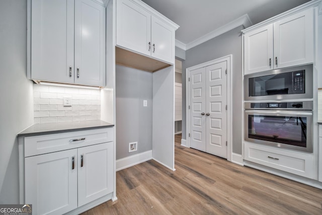 kitchen featuring light wood finished floors, ornamental molding, decorative backsplash, black microwave, and stainless steel oven